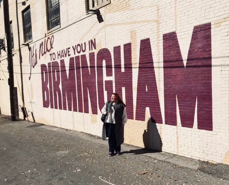Tetiana posing in front of a graffiti wall that reads: "It's nice to have you in Birmingham."