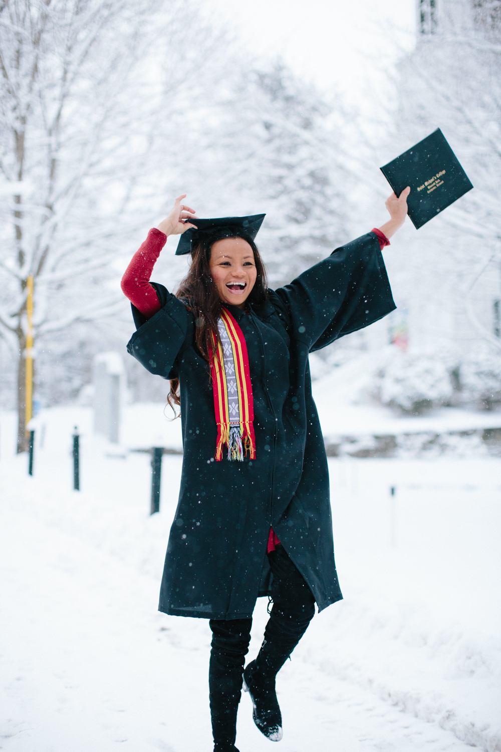 Raina, wearing a cap and gown, dancing in the snow with her diploma