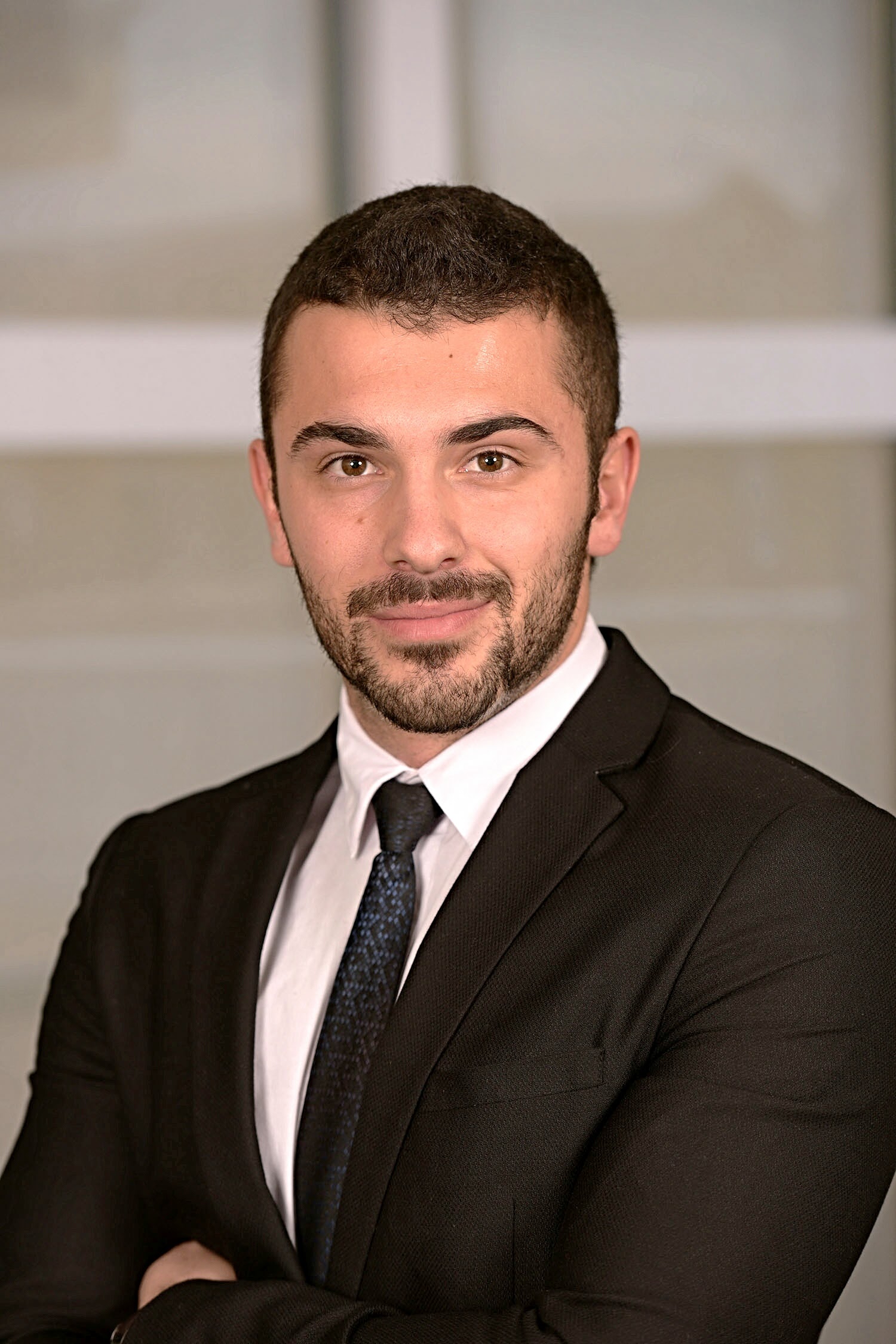 Egzon, posing for a professional headshot in a dark suit with arms crossed.